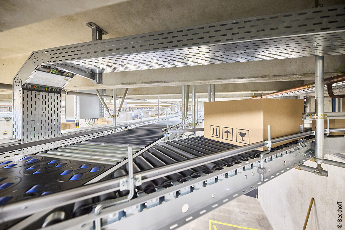 This approximately 250 m long central ring conveyor from Arvato SE was extensively modernized with PC-based control, One Cable Automation, and around 200 EP Box modules for roller drives.